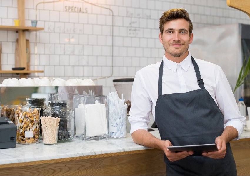 Happy male cafe owner in his cafe with a tablet in his hand