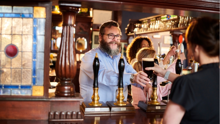 A pub landlord serving a customer from behind the bar